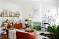 Living room with mid-century decor, orange sofa, wooden sideboard, plants, and a white fireplace with a mounted skull.