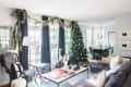 Living room with Christmas tree, garland, dark curtains, and a dining area with green chairs and a chandelier.