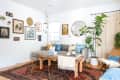 Cozy living room with a gray sectional, wooden coffee table, patterned rug, wall art, and a large potted plant.