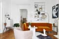 Living room with orange velvet sofa, white coffee table, pink armchair, and built-in shelves with decor and plants.