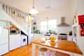 Bright kitchen with wooden floors, white cabinets, fruit bowl on island, and staircase leading to upper level.