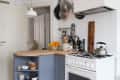 Cozy kitchen with blue cabinets, wooden countertop, hanging pots, fruit bowl, and a kettle on the stove.