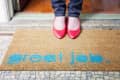Doormat with "great job" in blue text, person in red shoes standing on it.