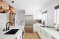 Modern kitchen with white cabinets, stainless steel fridge, copper pendant lights, and black sink faucet.