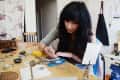 Woman crafting jewelry at a cluttered workbench with tools and materials.