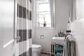 Small bathroom with striped shower curtain, toilet, sink with toiletries, and a window with potted plants.