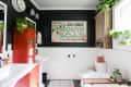 Bathroom with black walls, red cabinet, white sink, plants, and a vintage mouth soap sign.