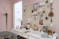 Home office with a white desk, mood board, decorative items, and a modern lamp against a pink wall.