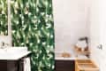 Bathroom with green leaf-patterned shower curtain, white sink, stacked towels, and wooden storage shelves.