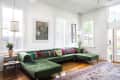 Living room with green velvet sectional sofa, colorful cushions, wooden floor, and large windows.