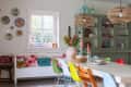 Colorful dining room with mismatched chairs, floral centerpiece, wall plates, and a green cabinet displaying dishes.