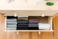 Open wooden drawer with neatly folded clothes in various colors and patterns on a hardwood floor.