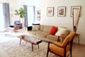 Mid-century modern living room with beige sofa, colorful pillows, wooden coffee table, Eames lounge chair, and framed art.