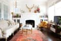 Eclectic living room with a white sofa, colorful rug, fireplace, and mounted bull skull, featuring bookshelves and a TV console.