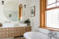 Modern bathroom with round mirror, double sinks, wooden vanity, white subway tiles, and a freestanding bathtub.