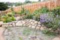 Garden with stone wall, colorful flowers, and wooden fence in the background.