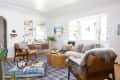 Cozy living room with a husky on a blue cushion, leather chairs, a wicker coffee table, and a sofa with patterned pillows.