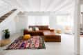 Living room with brown leather sectional, colorful rug, potted plant, and white armchair under a staircase.