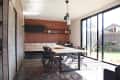 Modern kitchen with brick wall, wooden cabinets, dining table, black chairs, and large sliding glass doors opening to a garden.