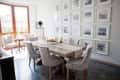 Dining room with a wooden table, beige chairs, fruit centerpiece, and a wall of framed photos.