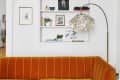 Orange velvet sofa in front of a white built-in bookshelf with art, plants, and a shell floor lamp.
