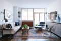 Modern living room with a beige sofa, Eames lounge chair, patterned rug, and plants on a wooden coffee table.