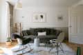 Cozy living room with a gray sofa, patterned cushions, rocking chair, small round tables, and framed art on the wall.