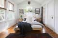 Bedroom with wooden bed, white bedding, plants on shelf, and two wooden nightstands with lamps.