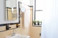 Small bathroom with beige tiles, white sink, and bathtub. A shower curtain, wall mirror, and potted plants on the window ledge.