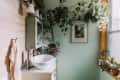 Bathroom with a round white sink, hanging plants, wooden wall, and framed art on a mint green wall.
