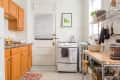 Small kitchen with wooden cabinets, white stove, metal shelves, and potted plants.