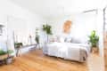 Bright bedroom with wooden floor, potted plants, a cozy bed, and wall art.