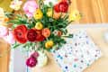 Colorful ranunculus bouquet in a vase on a table next to a book titled "Beaches."
