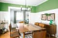 Dining room with green walls, wooden table, mid-century chairs, sideboard, and a bar cart.