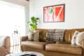 Living room with brown leather sofa, red patterned rug, round marble coffee table, and framed 1977 poster on the wall.