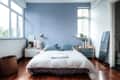 Bedroom with blue accent wall, double bed, blue pillows, wooden nightstands, and a large window.