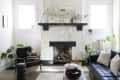 Living room with white stone fireplace, black sofa, armchair, plants, and a wooden coffee table.