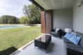 Covered patio with wicker furniture, blue cushions, glass table, and view of a grassy yard with a pool and trees.