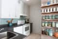 Modern kitchen with white cabinets, teal backsplash, and shelves of glass jars filled with spices and ingredients.