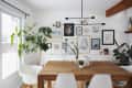 Dining room with wooden table, white chairs, large plant, and gallery wall of colorful framed art.
