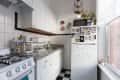 Small kitchen with white cabinets, checkered floor, fridge with photos, and a window with potted plants.