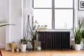Living room corner with potted plants, a black radiator, and a tall floor lamp by a large window.
