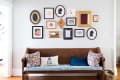 Wooden bench with floral cushions and a DC pillow, beneath a gallery wall of framed art and silhouettes.