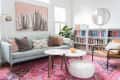 Living room with light blue sofa, colorful pillows, pink rug, round coffee tables, bookshelves, and cactus artwork.