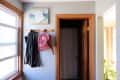 Coat and red backpack hanging on a wooden hook in a hallway with a window and a closed door.
