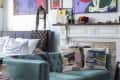 Living room with teal sofa, abstract pillows, white fireplace, and colorful artwork on the wall.