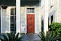 Red front door with number 1021, white wicker chair, and potted plants on a porch.