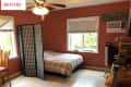 Bedroom with terracotta walls, bed with plaid bedding, folding screen, ceiling fan, and window AC unit.