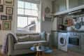 Cozy kitchen-living area with a gray sofa, wall art, washing machine, and kitchen appliances under green cabinets.