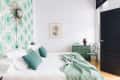 Bedroom with green patterned wallpaper, white bedding, green pillows, a green dresser, and a black door.